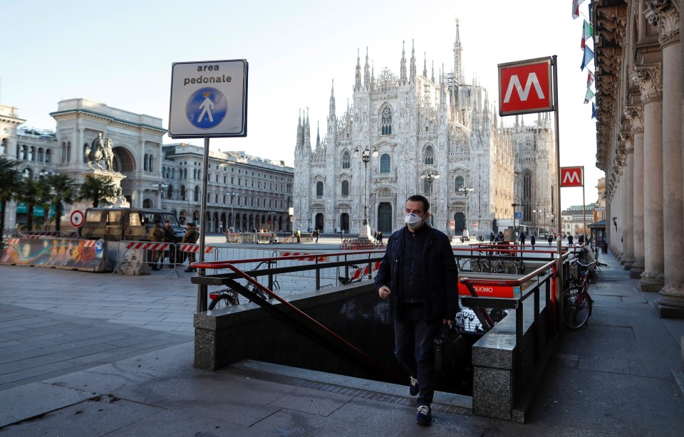  A man in a mask walks out of a Milan metro station into an eerily empty Duomo Square