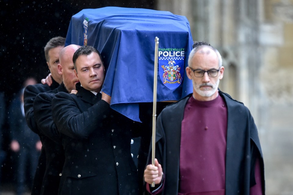 Clergy lead the pallbearers as they carry the coffin of PC Harper