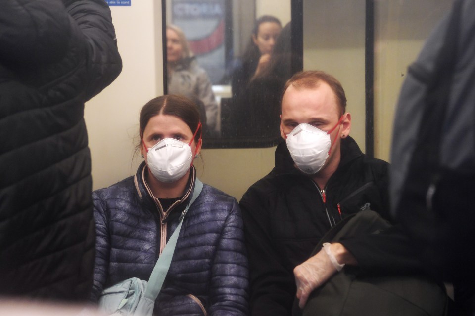  A couple wear medical face masks and plastic gloves while sitting on the Underground in London