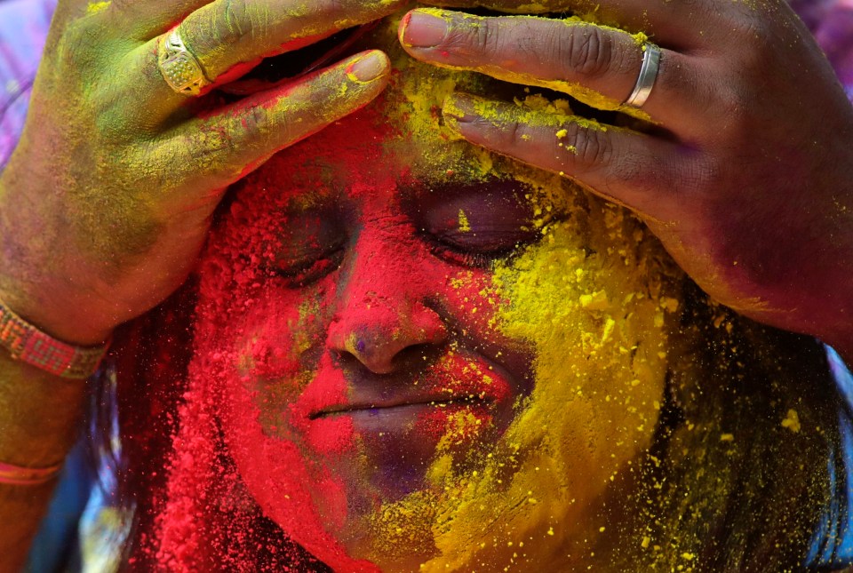 A woman coats her face in coloured powder during the celebrations in Mumbai, India