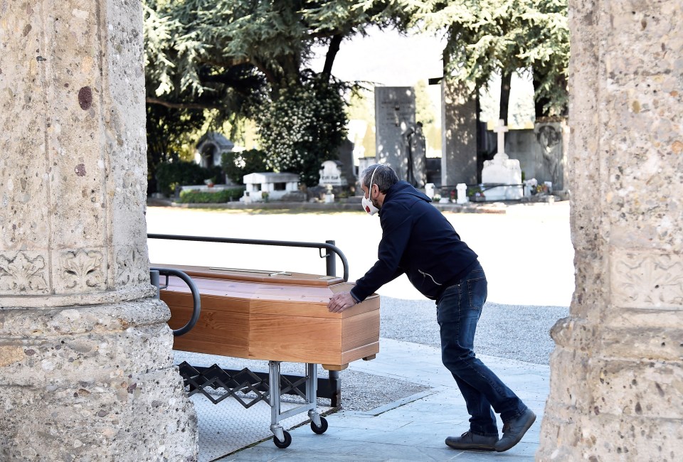  A man in a protective mask transports a coffin inside a cemetery in Bergamo