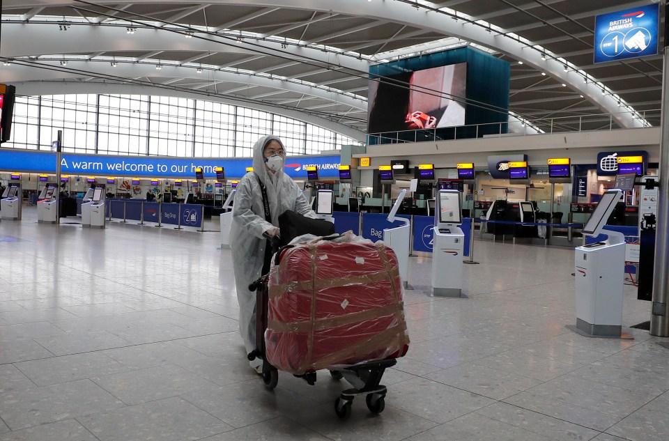  A traveller in protective clothing carries her luggage at Heathrow Airport