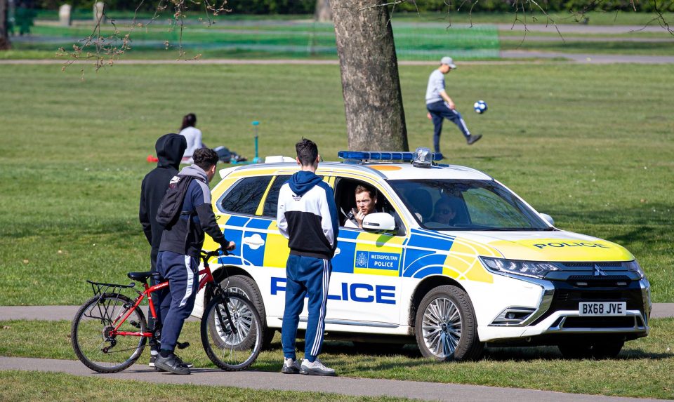  A police officer enforcing strict social distancing measures speaks to three lads in Greenwich Park