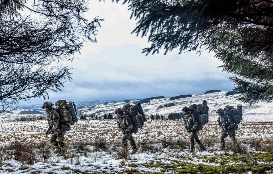  Soldiers trudging through the snow wearing heavy backpacks in the Sennybridge Training area in Wales