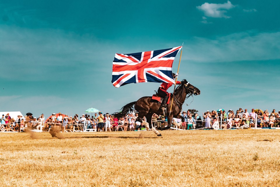  A member of the Household Cavalry holds a Union Jack aloft as he rides a horse at the open day at Bodney Camp, Norfolk