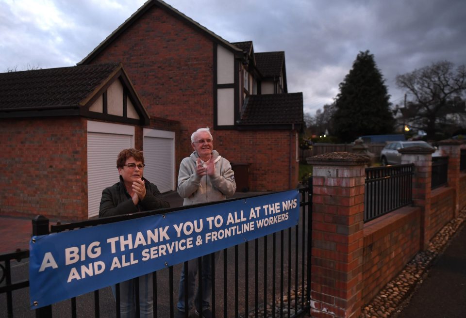  Two people stood and clapped behind a sign put up thanking all service and frontline workers