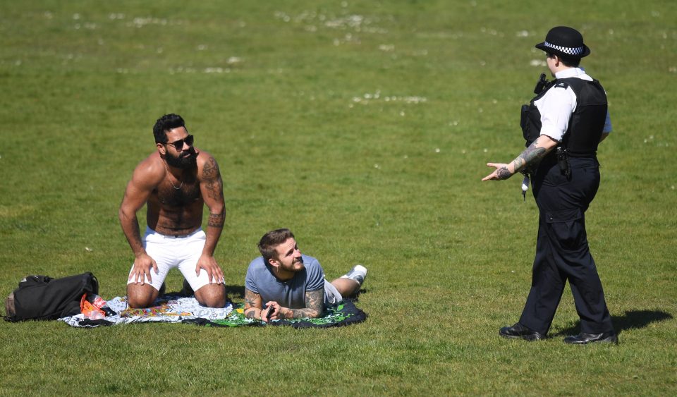  A police officer speaks to people sunbathing in Greenwich Park in London