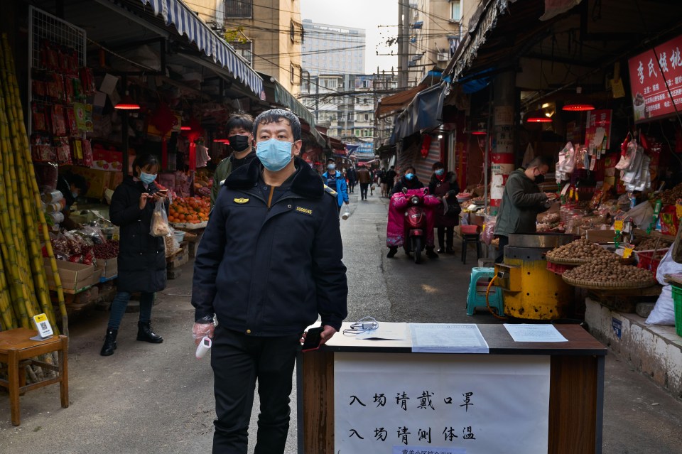 A security guard with a face mask outside a local seafood market for temperature screening