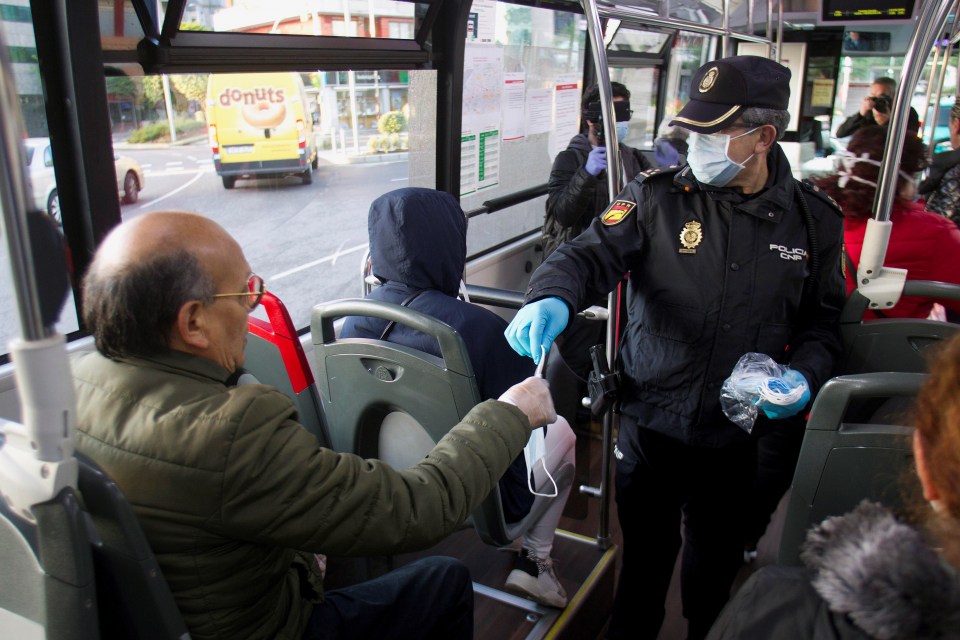  A police officer hands a mask to a commuter returning to work in Vigo, northwestern Spain