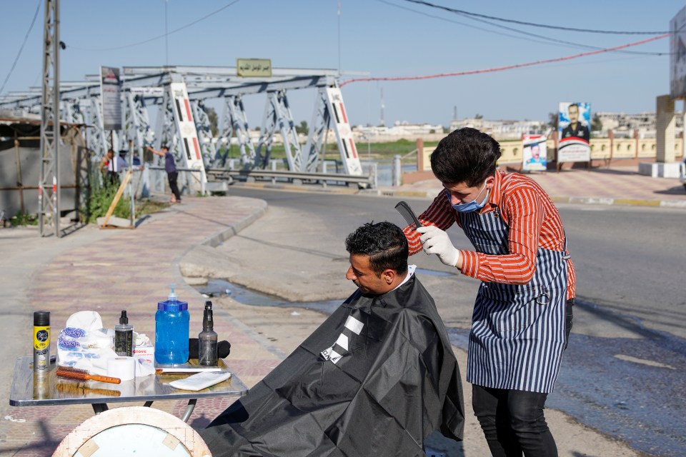  A barber wearing a protective face mask and gloves cuts the hair of a policeman in Mosul