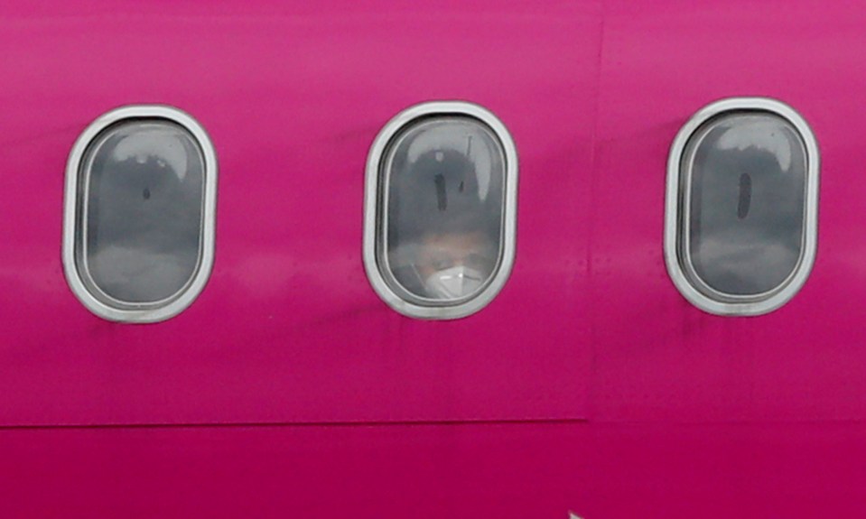  Passengers wearing masks peer out of the windows of a flight