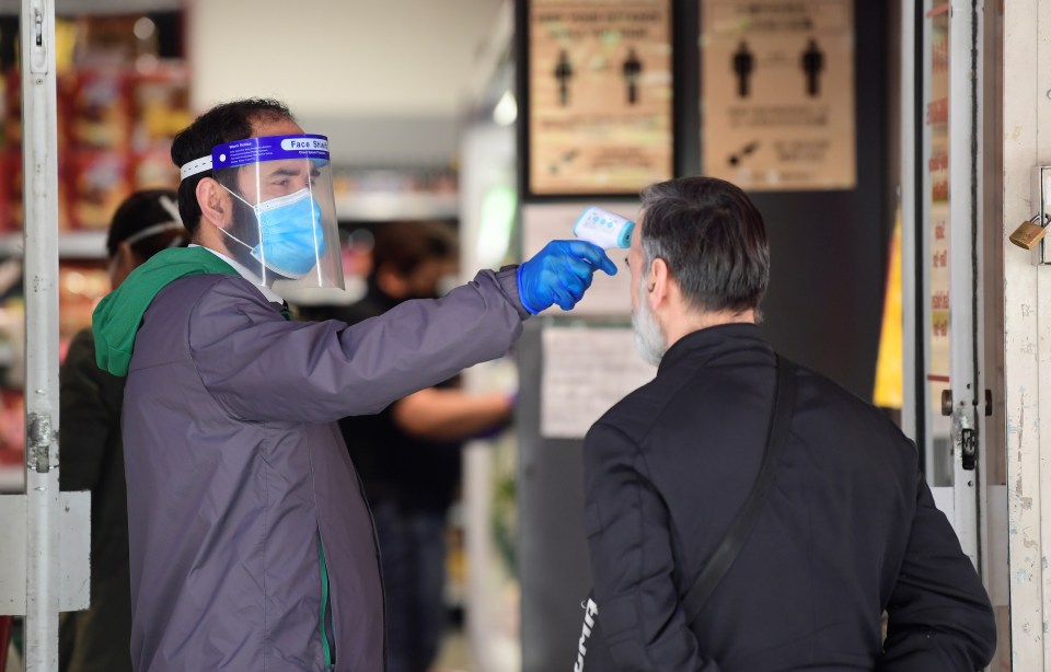  An employee takes the temperature of a customer at the entrance of a super market in China Town in London