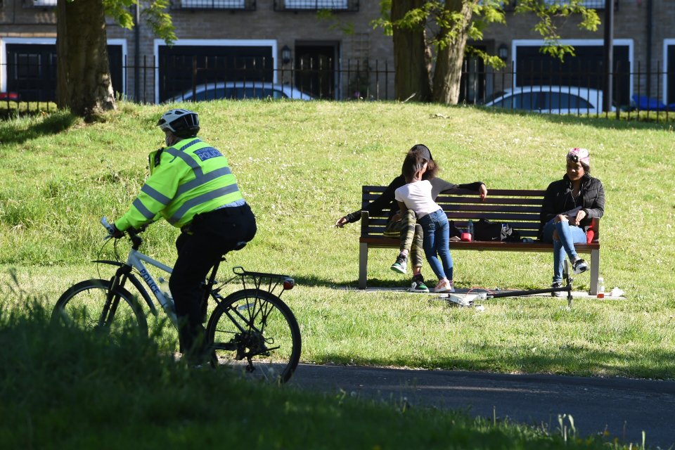  A police officer cycles past two people sitting on a park bench in lockdown