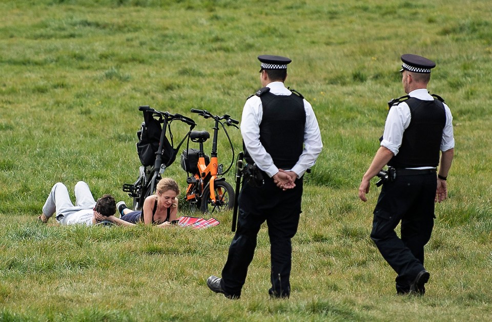  Police officers talk to members of the public lying down on Primrose Hill in North London