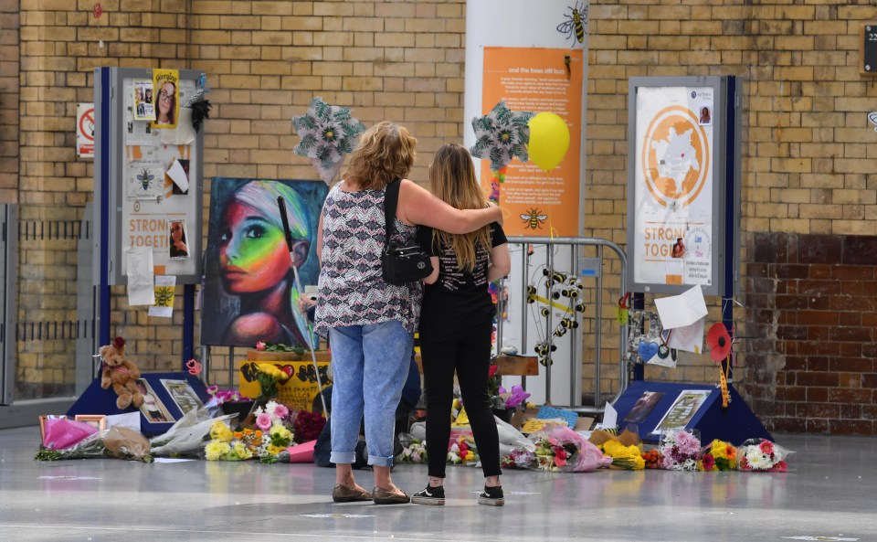 A woman comforts her daughter as they stand in front of the memorial for the 22 lives lost