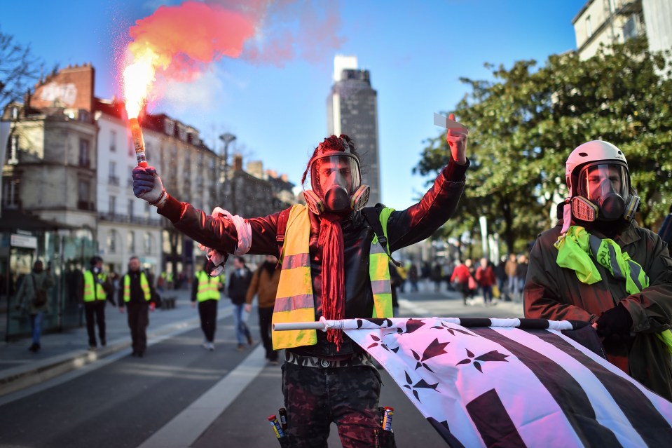  A protester holds a flare and gives the finger next to a Brittany's regional flag during a demonstration called by the 'Yellow Vests' ('Gilets Jaunes') movement in Nantes, western France, on February 2, 2019