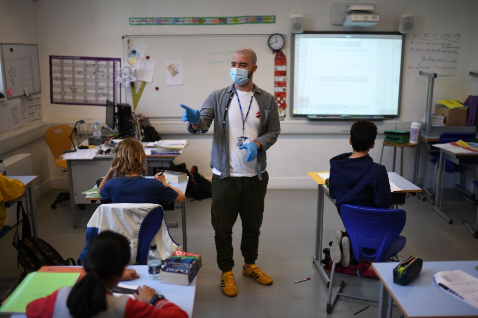  A teacher wearing a face mask teaches Year 6 pupils in a classroom with other pupils participating by video conference at a school in north London