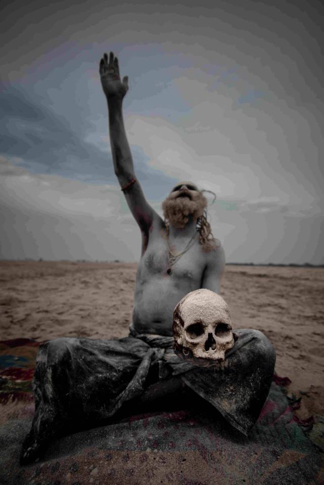  An Aghori man raises his hand while balancing a human skull on his lap