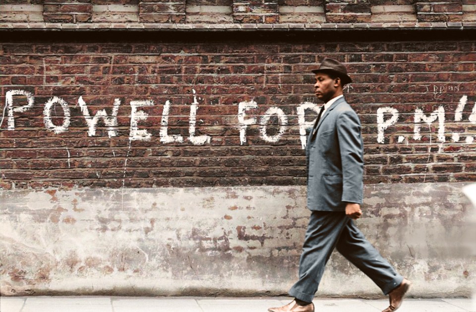 A black man walks past 'Powell for PM' graffiti, alluding to the controversial former MP Enoch Powell who spouted divisive views on black immigration and delivered the infamous 'Rivers of Blood' speech