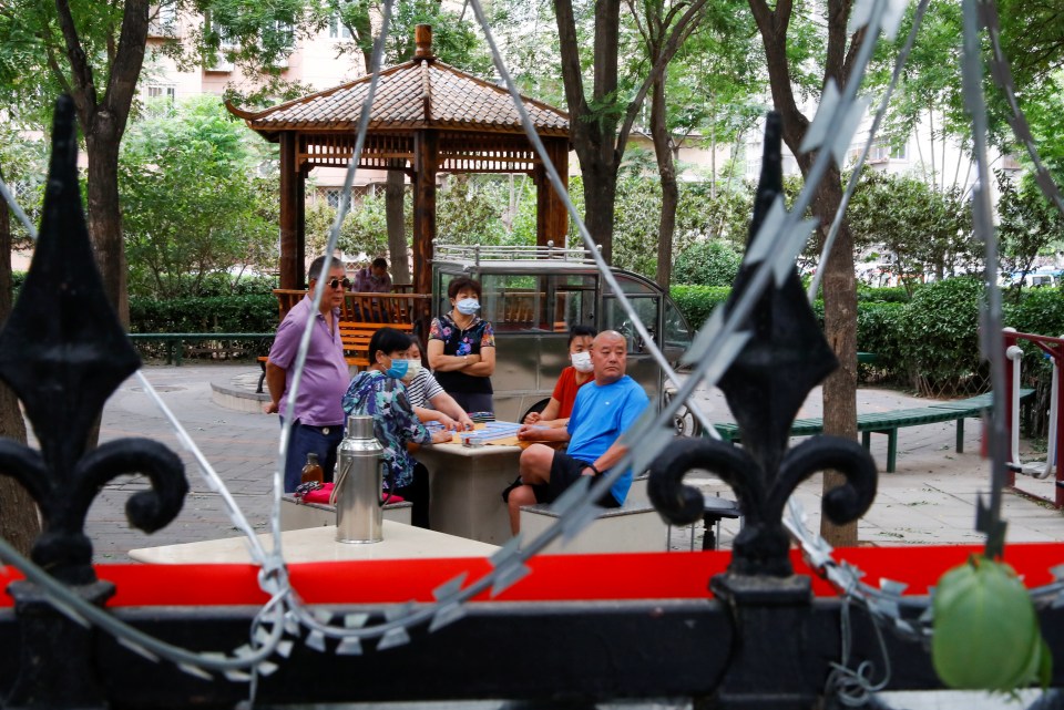 A group of people play mahjong inside a residential compound surrounded by razorwire