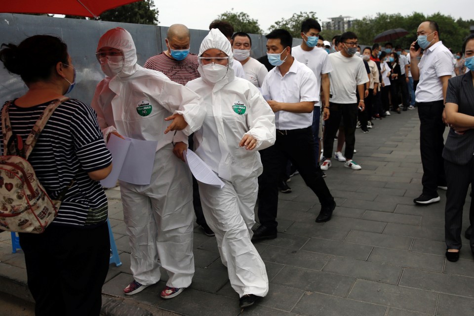 Medical workers in protective suits attend to those lining up outside a site for nucleic acid tests