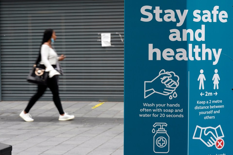 A woman walks past a sign urging people to stay safe