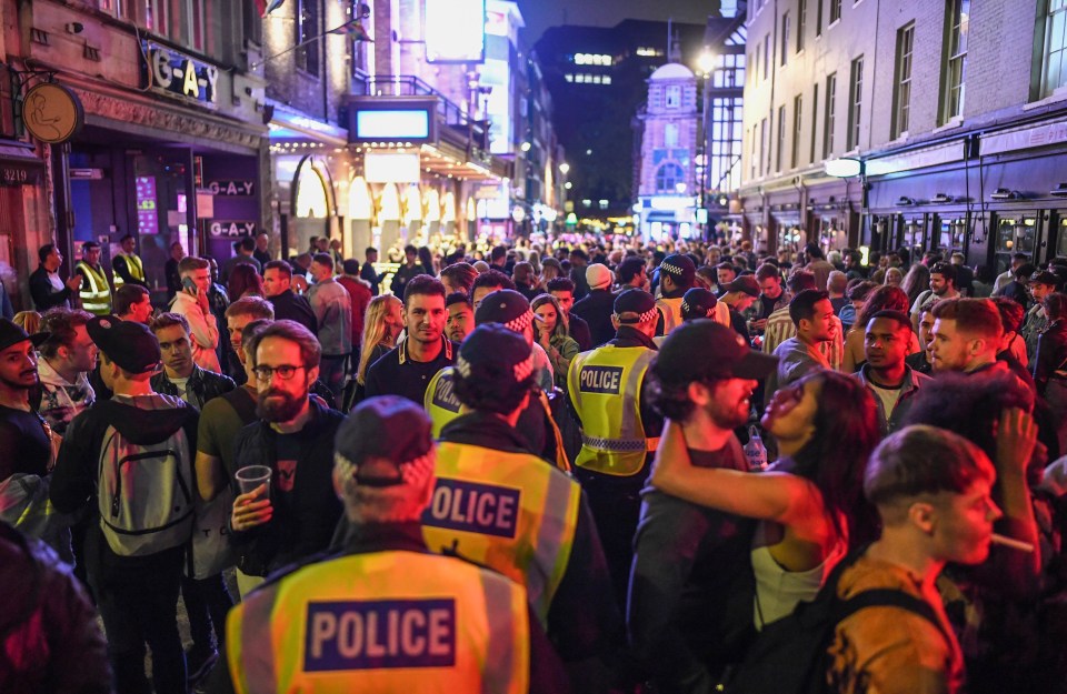 Police officers are seen walking through heavy crowds in Soho