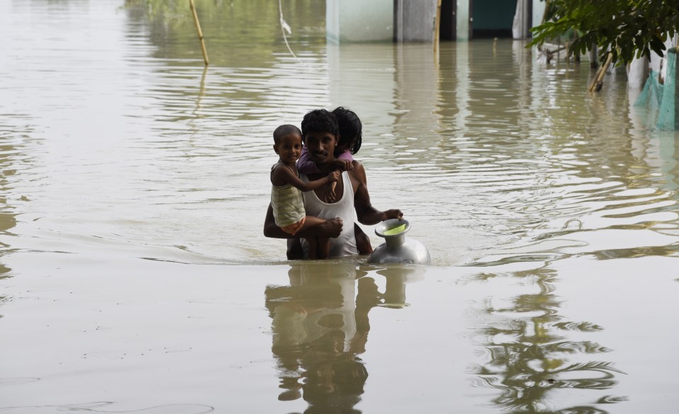 A man carries his children to a safer place in a flood-affected village of Kamrup district of Assam, India