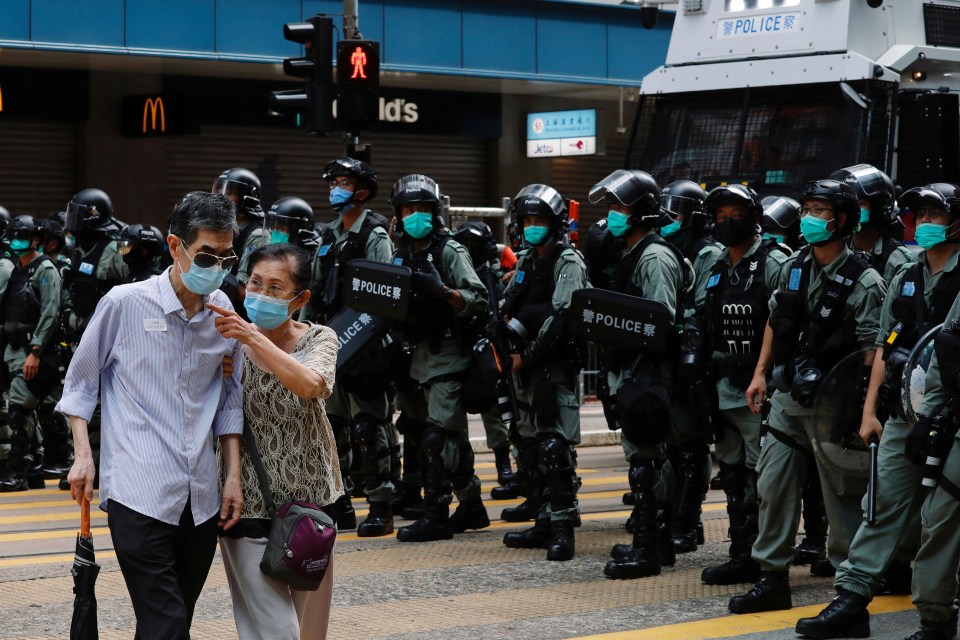 A couple walks past riot police as anti-national security law protesters march during the anniversary of Hong Kong's handover to China