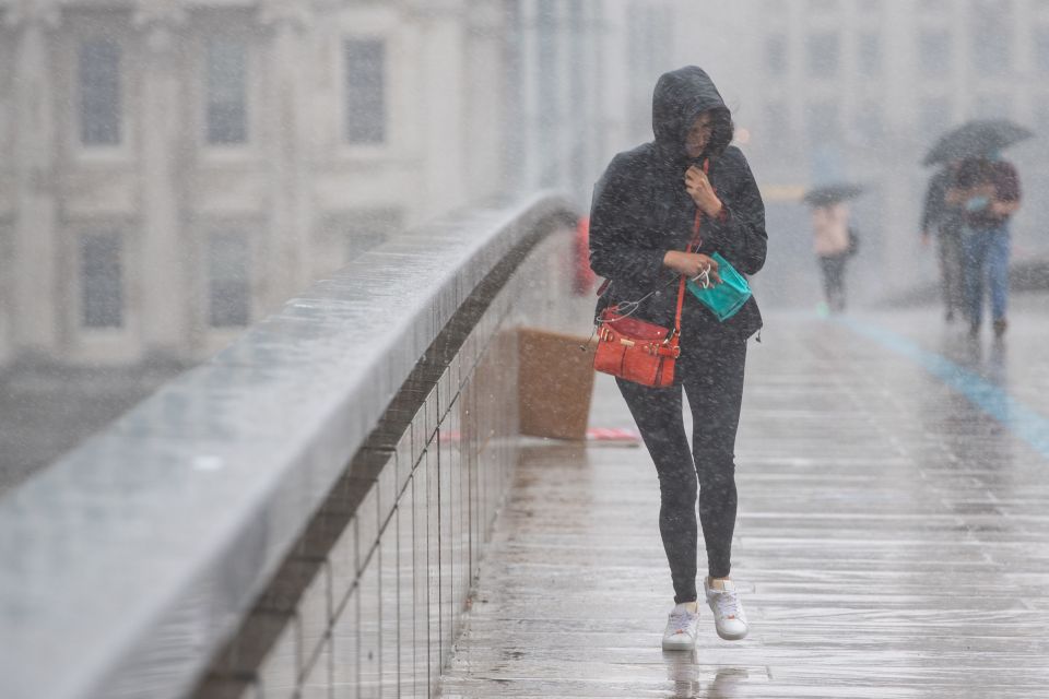 A woman runs to take shelter from poor weather on London Bridge yesterday