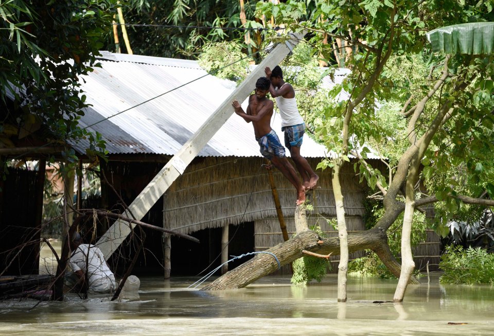 Men hold an uprooted electric pole, at a flood-affected village in Morigaon district of Assam in India