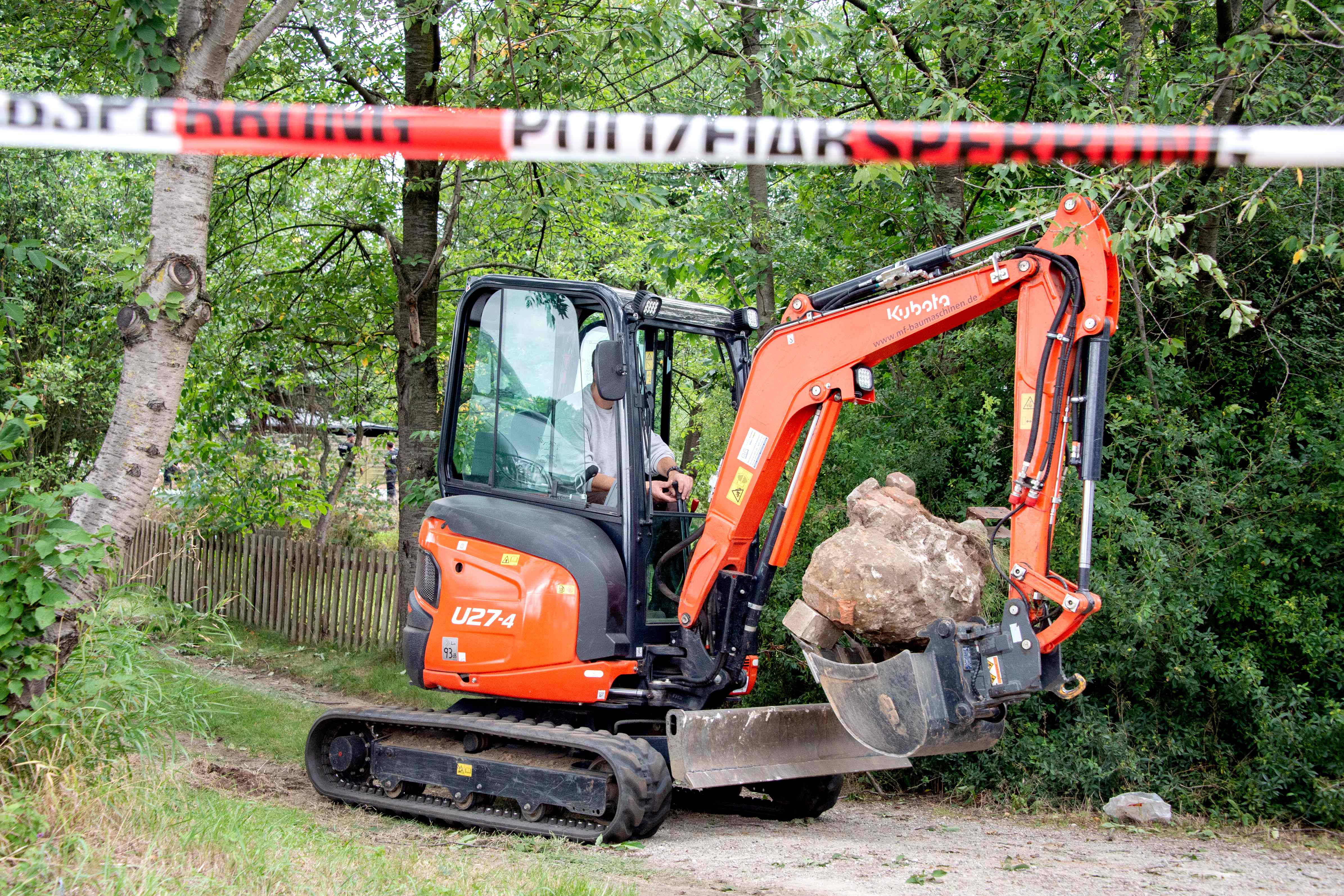 An excavator removes stone as police officers search the garden allotment 