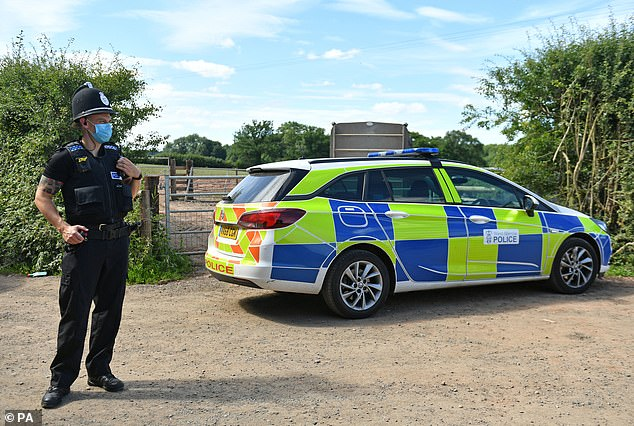 A police officers wearing a protective mask guards a gate of the Covid-19-hit farm in Herefordshire