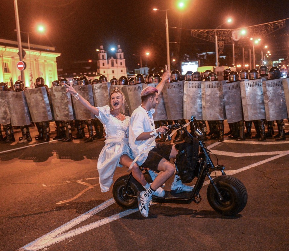 A young couple on a motorbike in front of the riot police