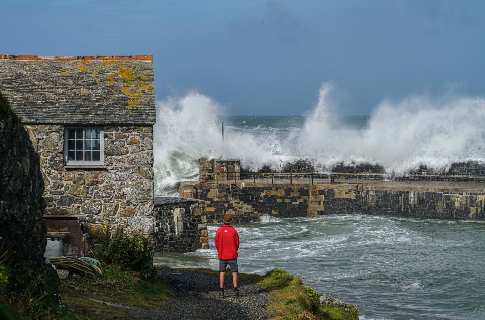 National Trust ranger Seth Jackson looks on as large waves caused by Storm Ellen strike Mullion Dove, Cornwall