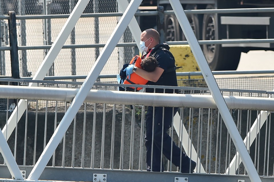 A young child is carried up the gangway by officials