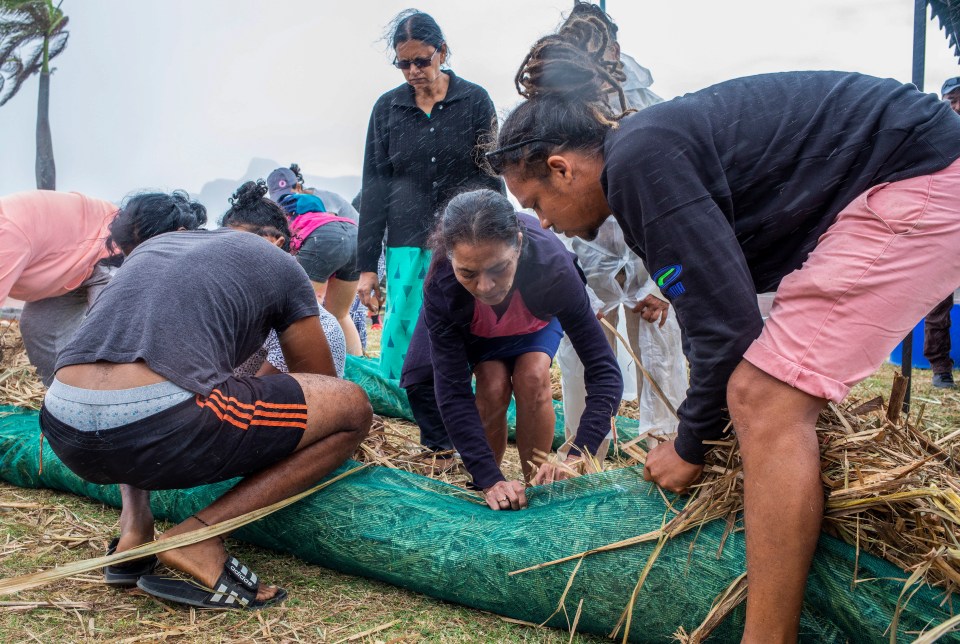 Local volunteers make absorbent barriers of straw stuffed into fabric sacks to contain oil from the MV Wakashio