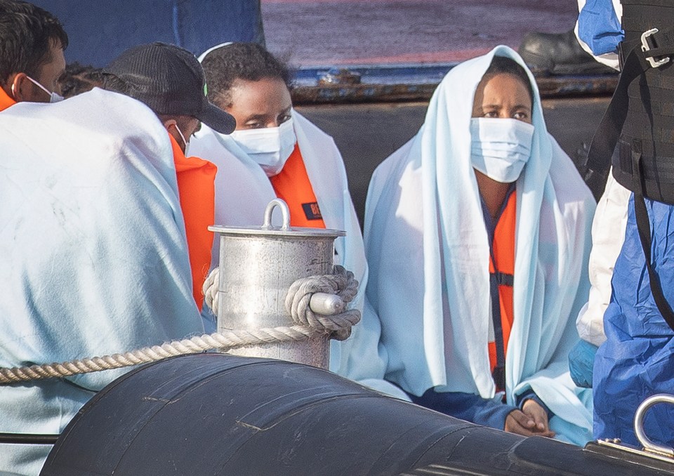 Migrants wrapped in blankets wait to be brought ashore by Border Force officials