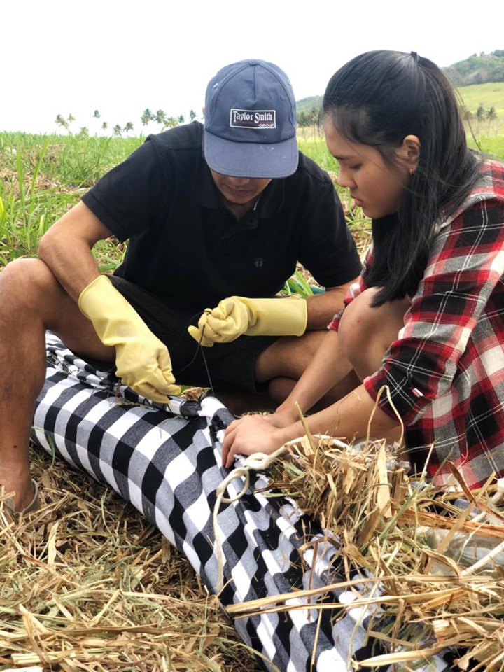 Volunteers making absorbent barriers of straw stuffed into fabric sacks, which are then sewn shut, to help contain the toxic sludge in Mauritius