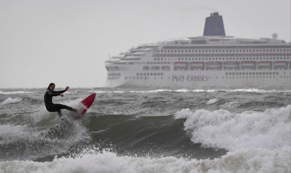 A surfer takes on the big waves as a ferry makes its way through the choppy sea