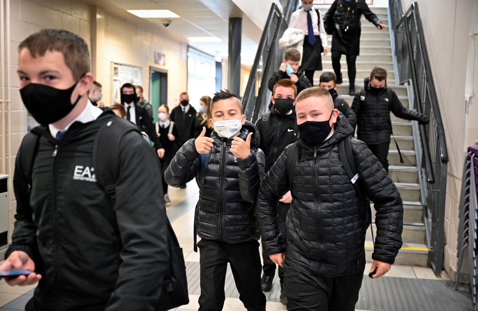 A boy gives a thumbs-up as he and his friends wear masks for the first time in school