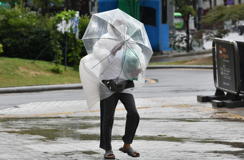 A woman holds an umbrella to shield herself from the powerful winds