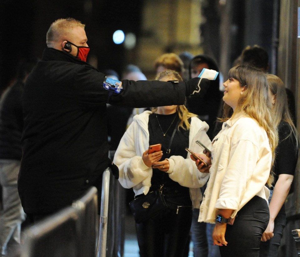 A doorman checks a reveller's temperature outside a bar