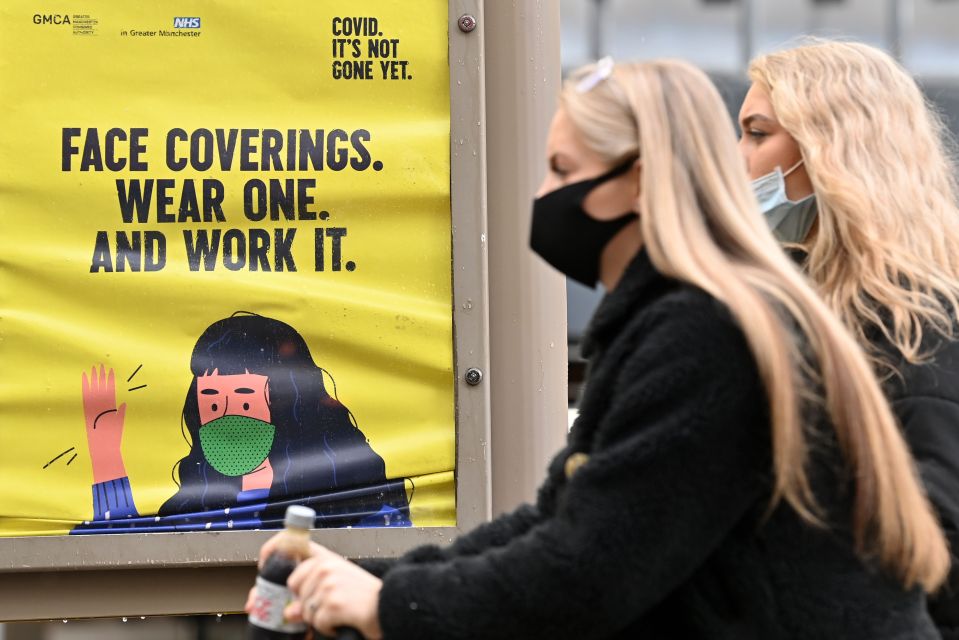 Women in Manchester stand by a sign instructing them to wear face masks