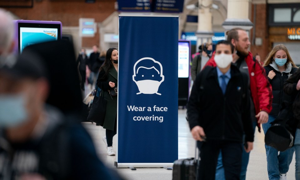 Passengers walk past a sign warning them to wear a face covering at Victoria St, London