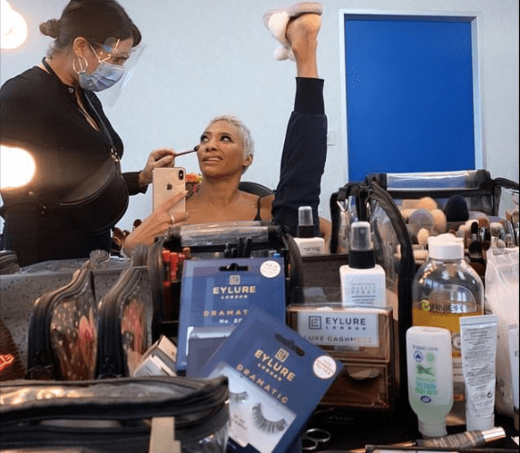 Karen being made up with the artist wearing a mask