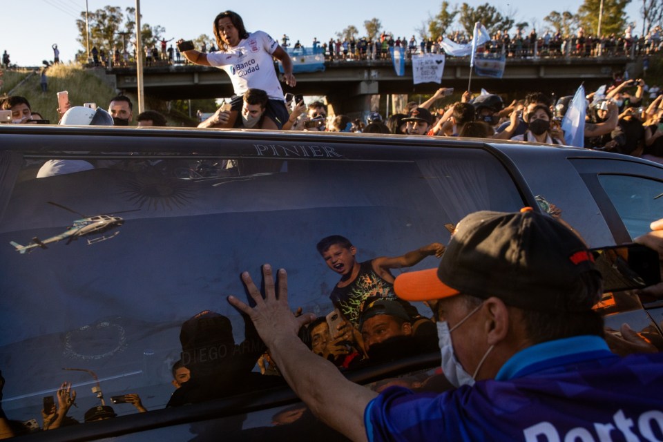 A grieving football fan puts his hand on the window of the hearse carrying Maradona’s coffin