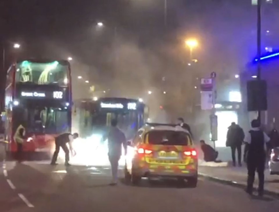 A man was arrested at the scene (near bus stop, right), say Met Police, after flames were extinguished in front of onlookers (left)