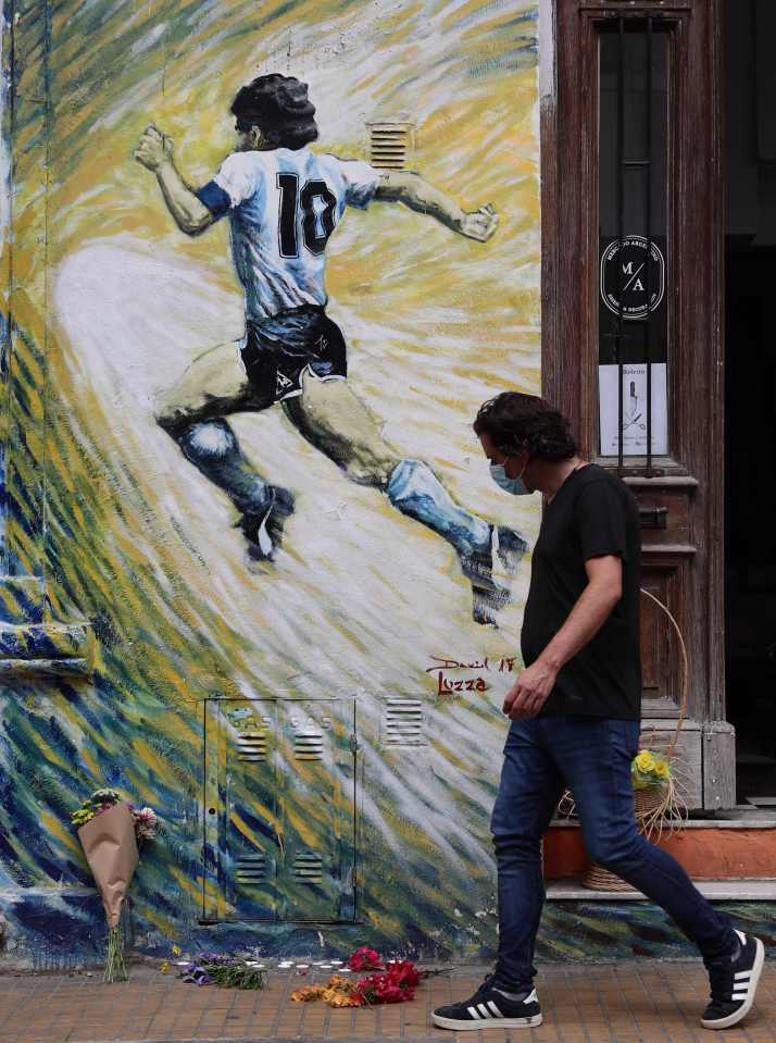 A man walks past flowers left by a mural of the revered legend in Argentia