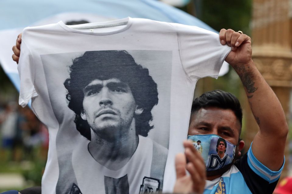 A man holds a shirt as fans wait to enter the Government House to pay tribute to late footy legend